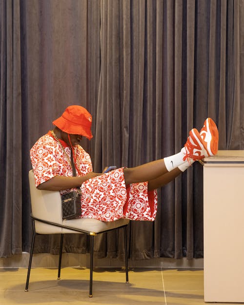 A man in red shoes and a hat sitting on a chair