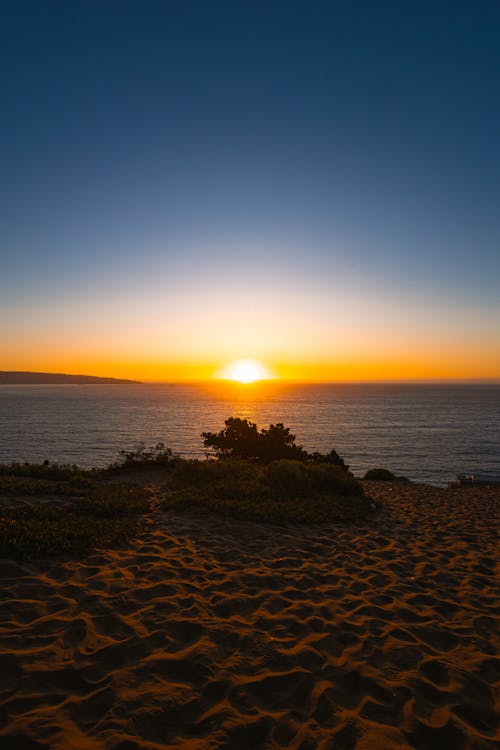 The sun sets over the ocean and sand dunes