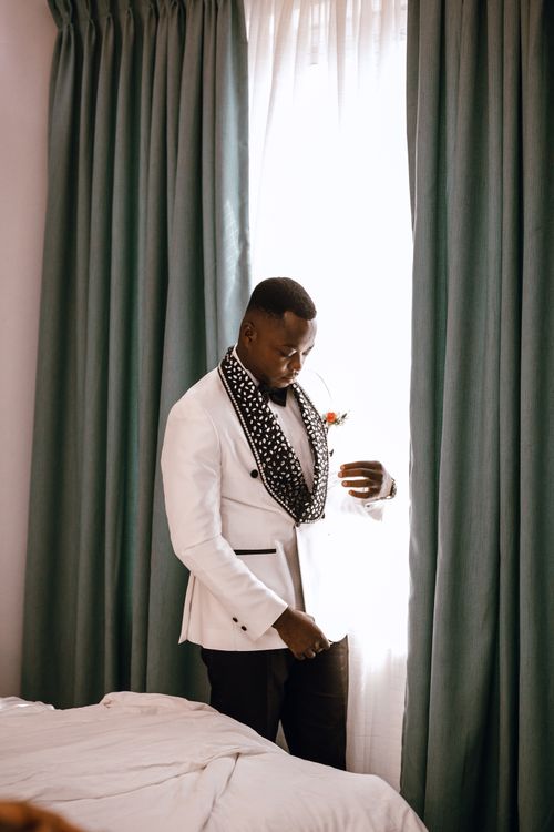 Free Man in a white suit stands thoughtfully by a window with curtains. Stock Photo