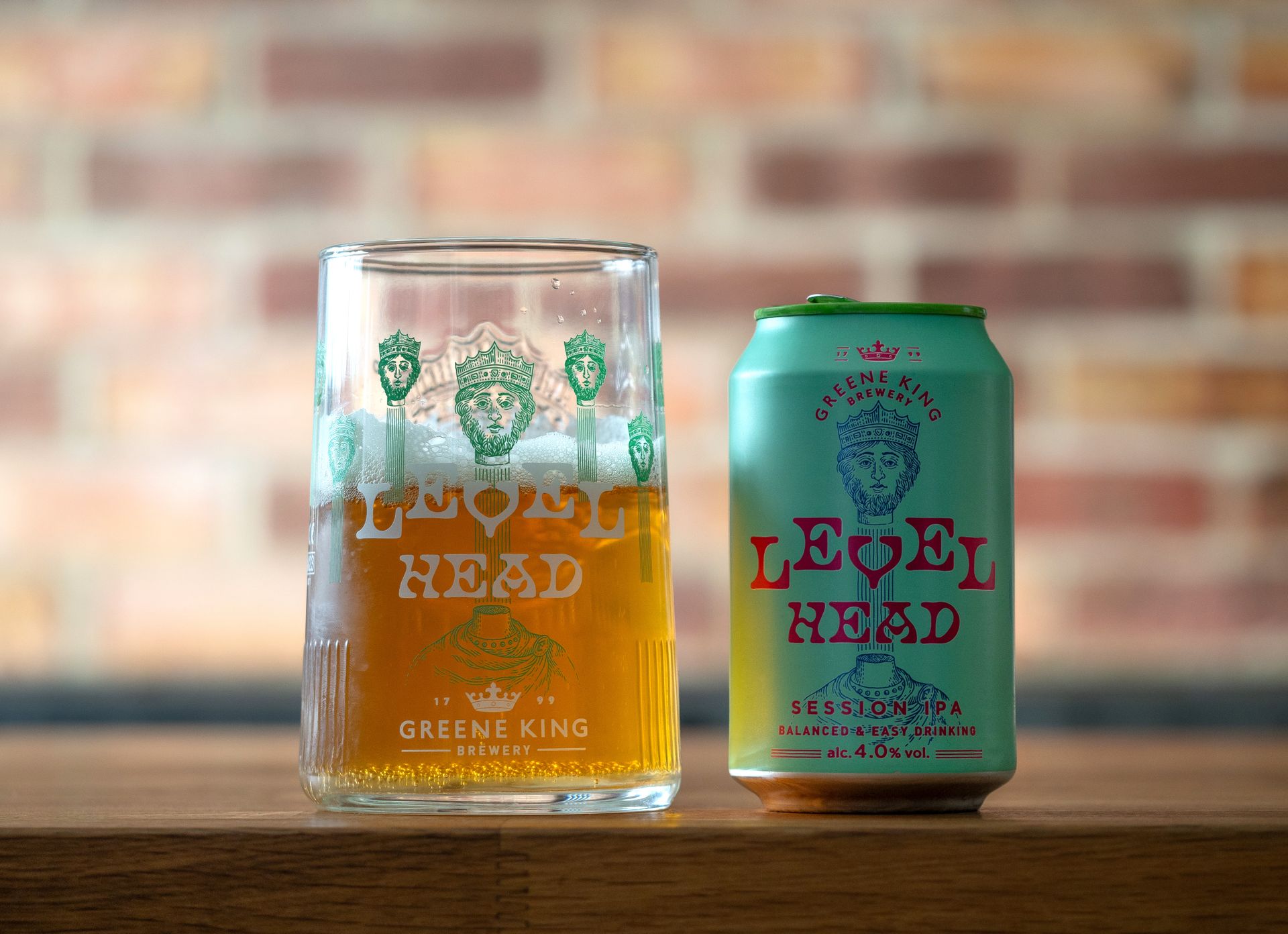 A refreshing glass and can of Level Head Session IPA from Greene King Brewery against a brick wall.