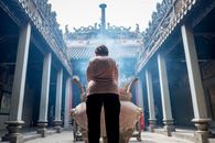 白天，一位女子在华丽亚洲寺庙的庭院里焚香祈祷