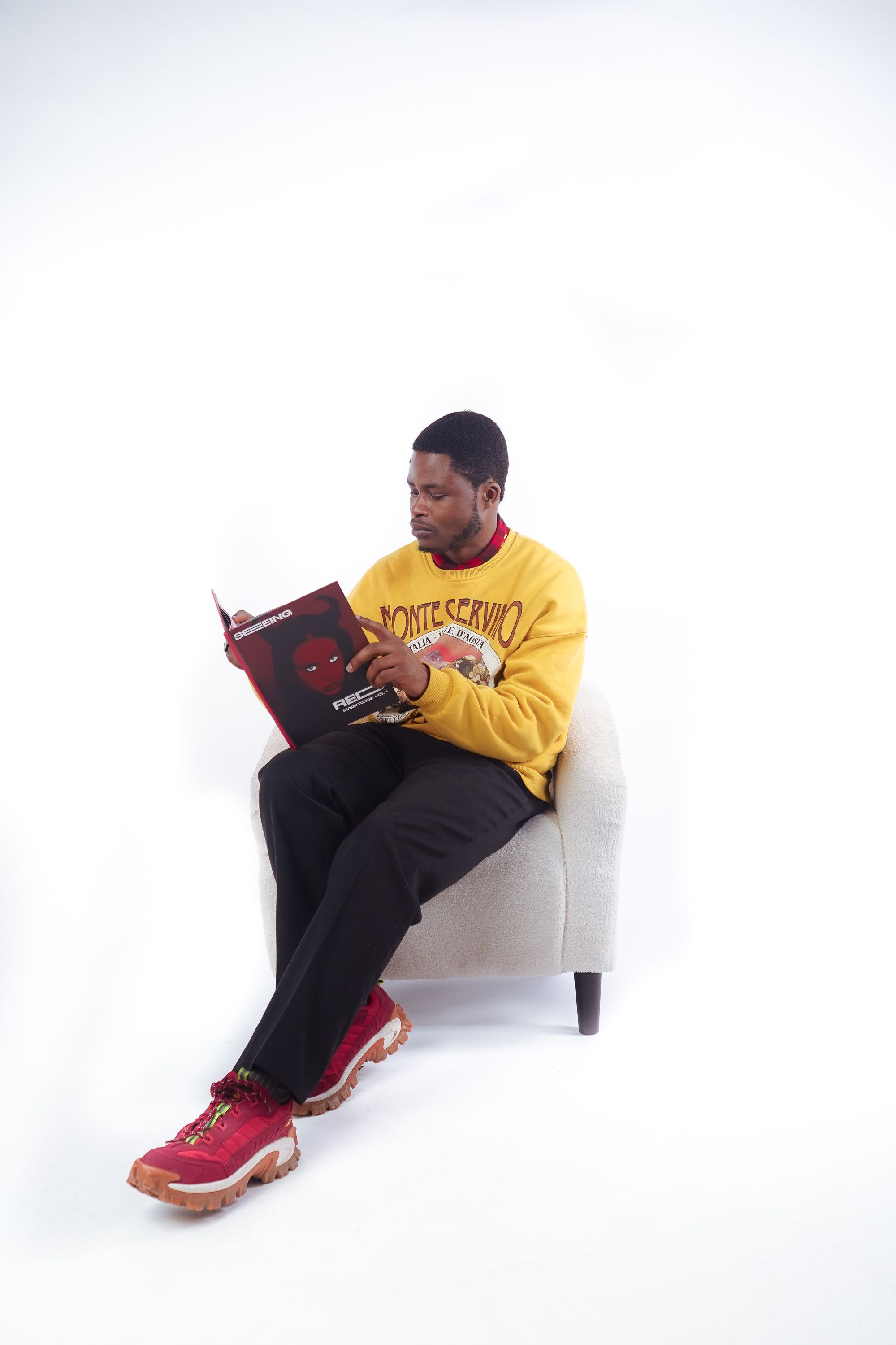 A stylish man in a yellow sweatshirt reads a comic book in a modern studio setting.