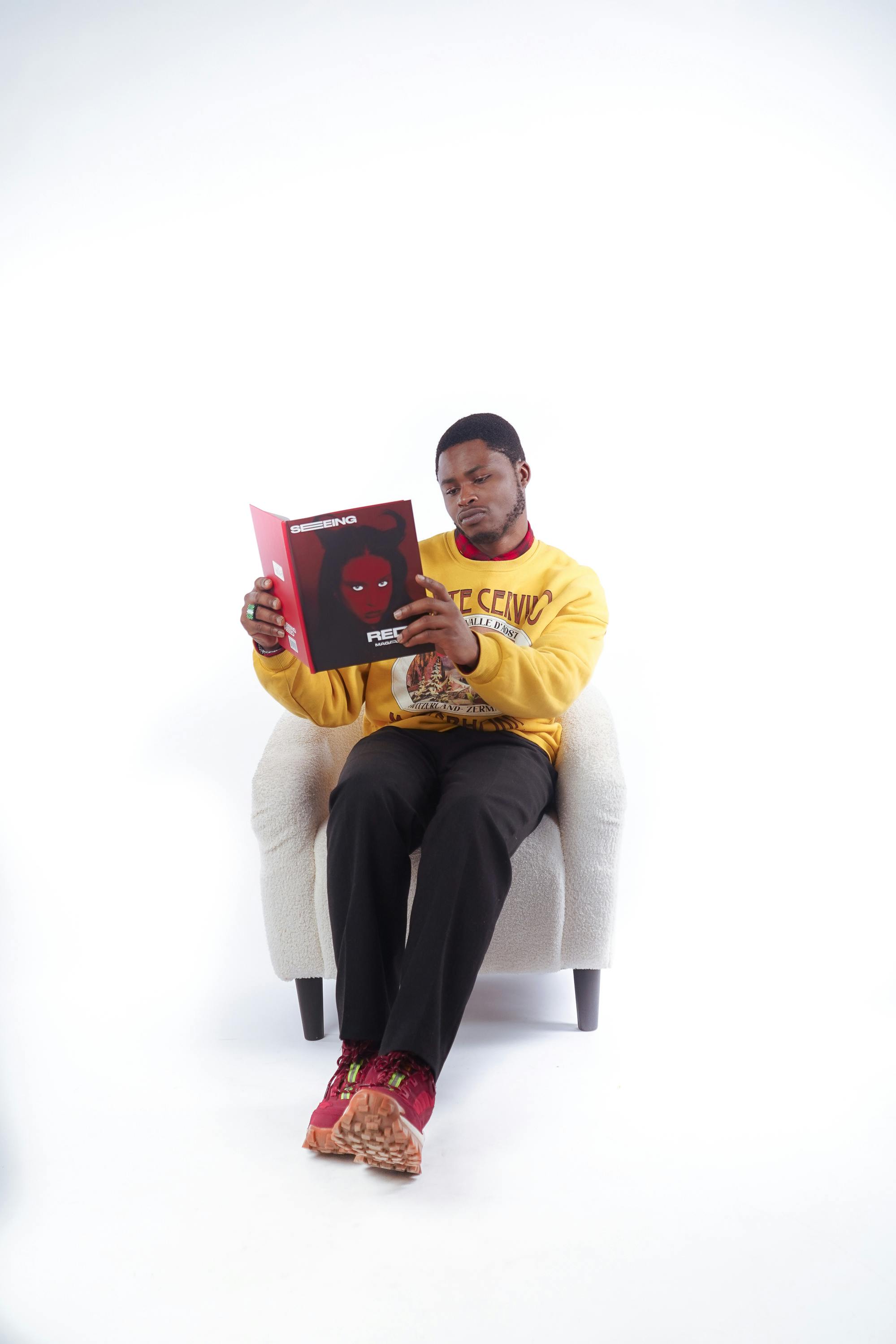 Free Young man in yellow sweatshirt reading a comic book, relaxing in a studio setting. Stock Photo