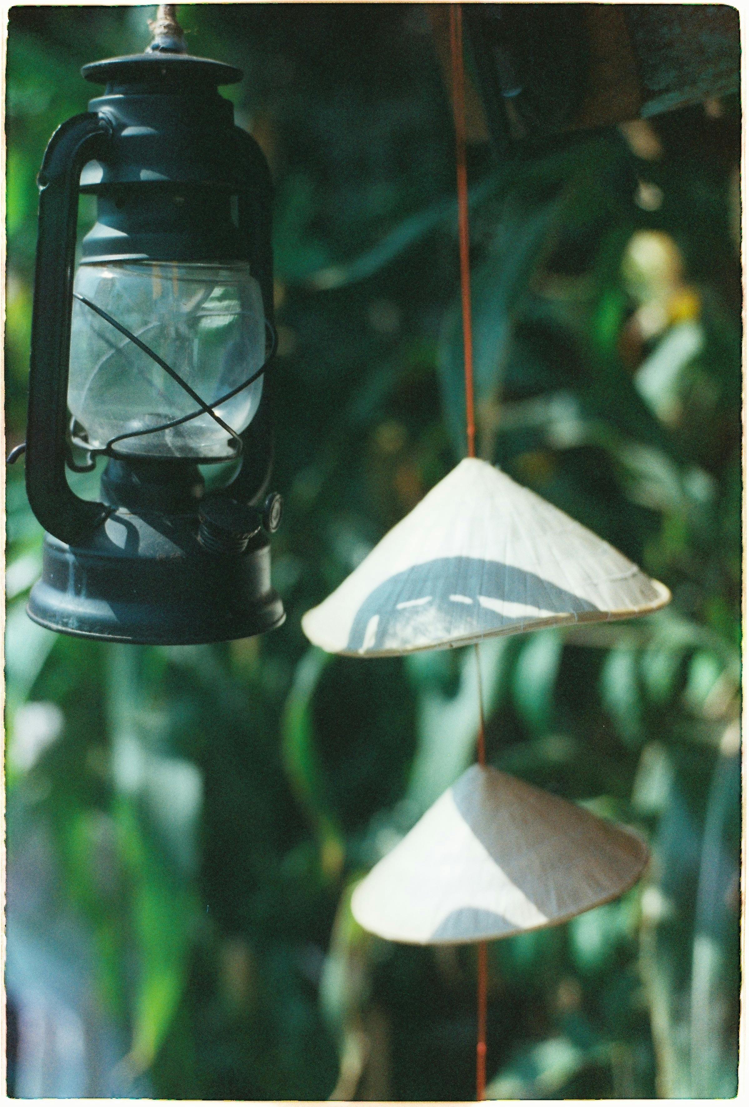 Vintage lantern and conical hats create a nostalgic scene outdoors with a blurred leafy background.
