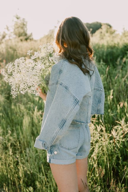 A woman in denim shorts and jacket holding a bouquet in a sunlit field, capturing summer vibes.