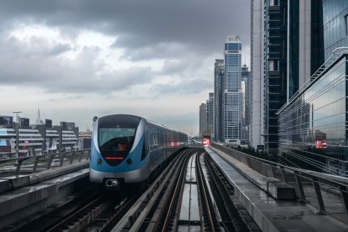 Free A sleek metro train travels through Dubai's urban skyline featuring towering skyscrapers under overcast skies. Stock Photo