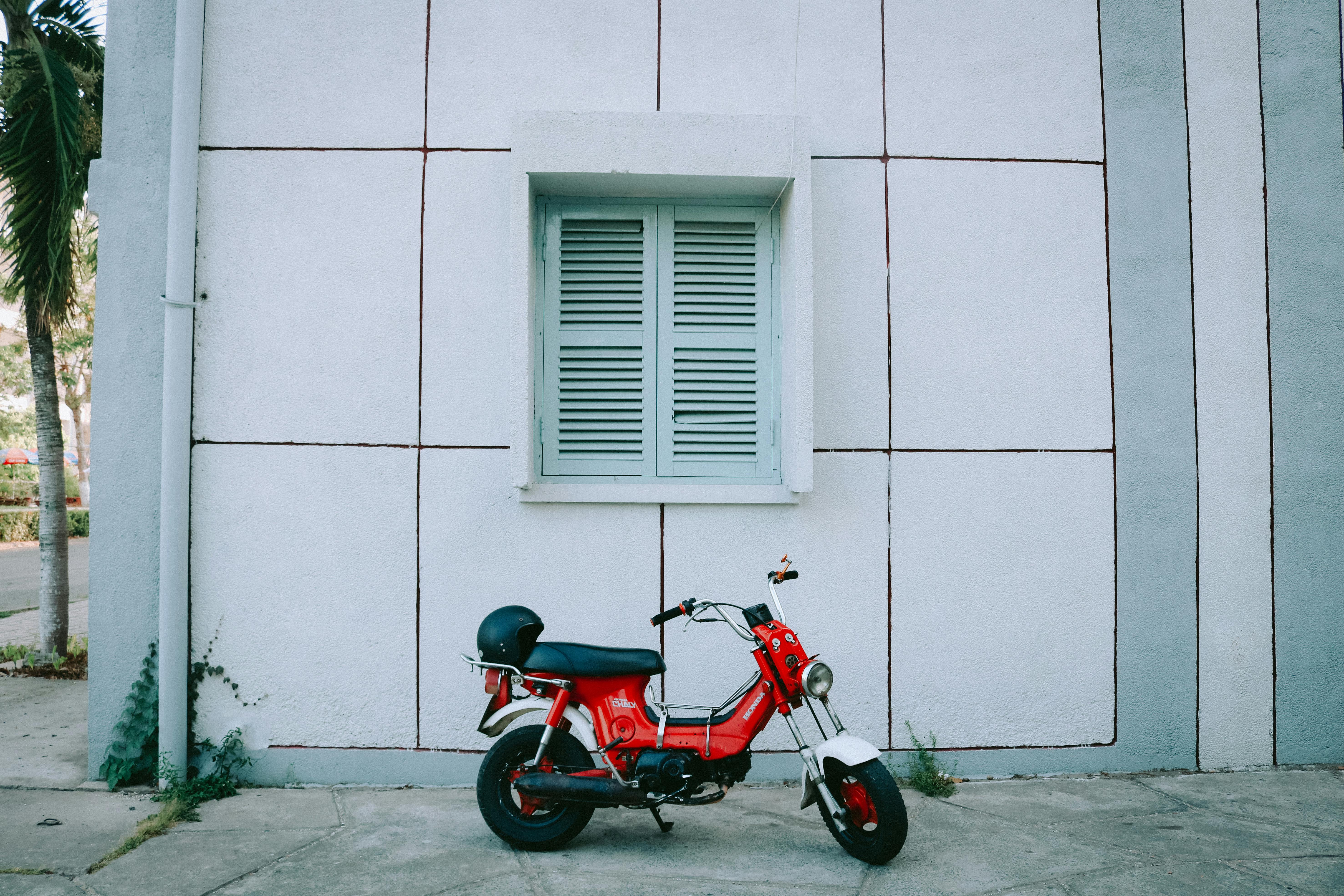 A red vintage motorcycle parked by a windowed wall on an urban street in Vietnam.