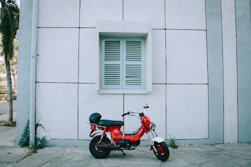 Red Motor Scooter Parked Beside White Concrete Building