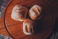 Top view of fresh artisan bread rolls on a wooden tray, perfect for food photography and culinary themes.