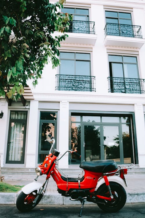 Red Motor Scooter Parked Beside White Concrete Building