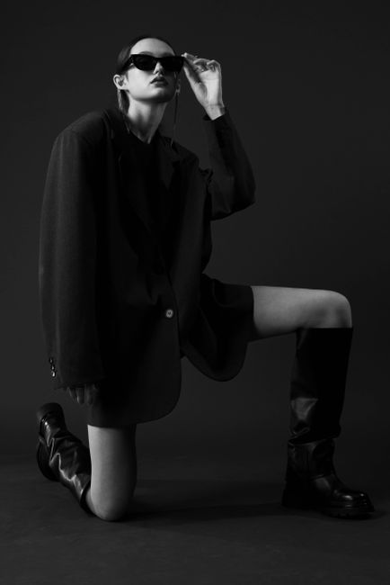 Elegant black and white portrait of a woman in boots and jacket, posing in studio.