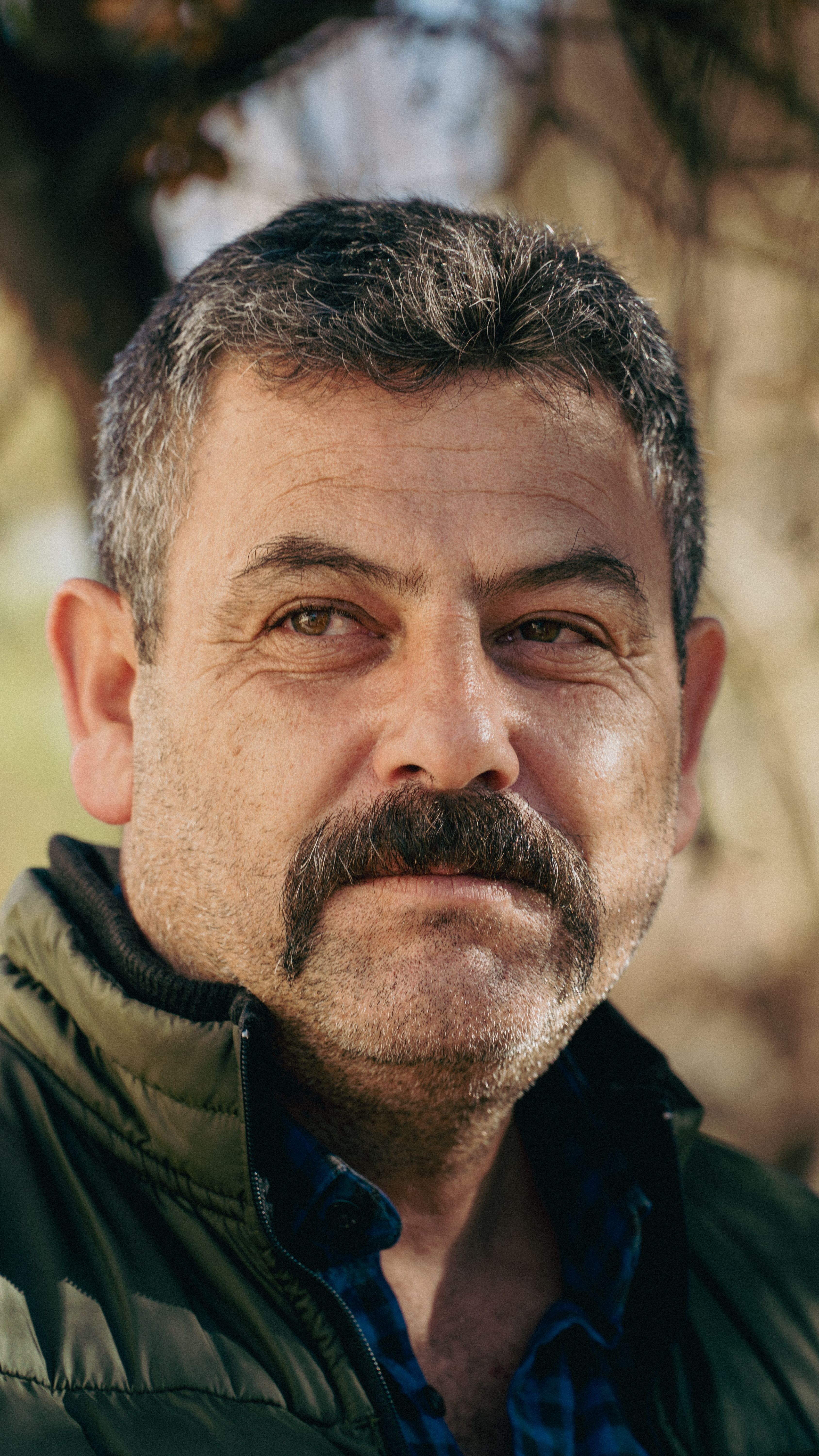 Close-up portrait of a mature man with facial hair, looking thoughtful outdoors.