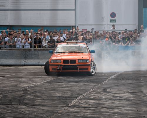 Free Orange car performing a thrilling drift in front of a crowd at an outdoor event. Stock Photo