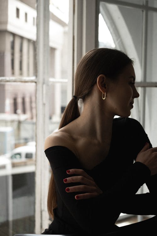 A woman in a black top and black pants sitting by a window