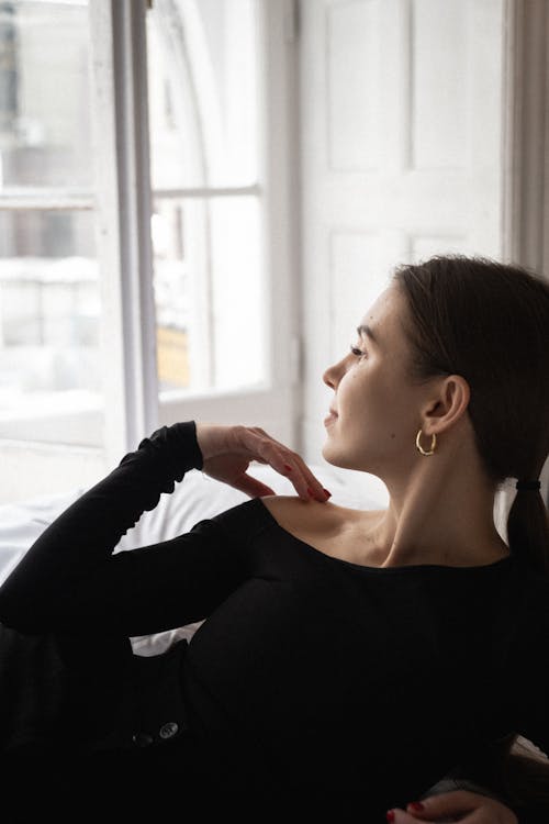 A woman in a black top and black pants is looking out the window