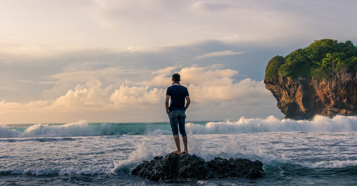Man Standing on Stone Near Seashore during Sunrise