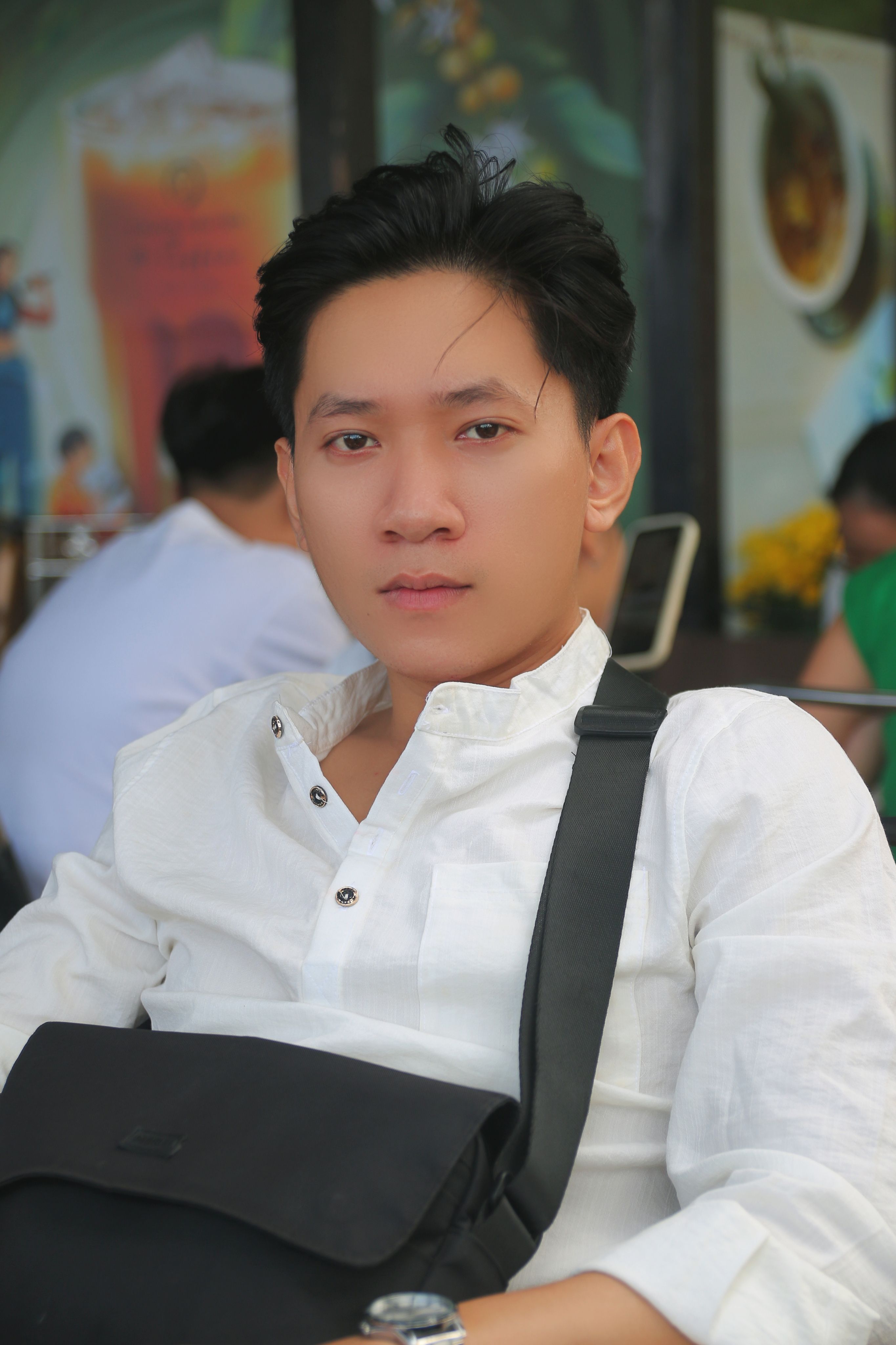 Casual portrait of a young man wearing a white shirt and carrying a black bag.
