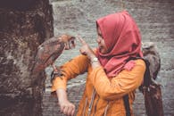 在乡村环境中，一名戴着头巾的妇女正与栖息在她手臂上的猫头鹰互动