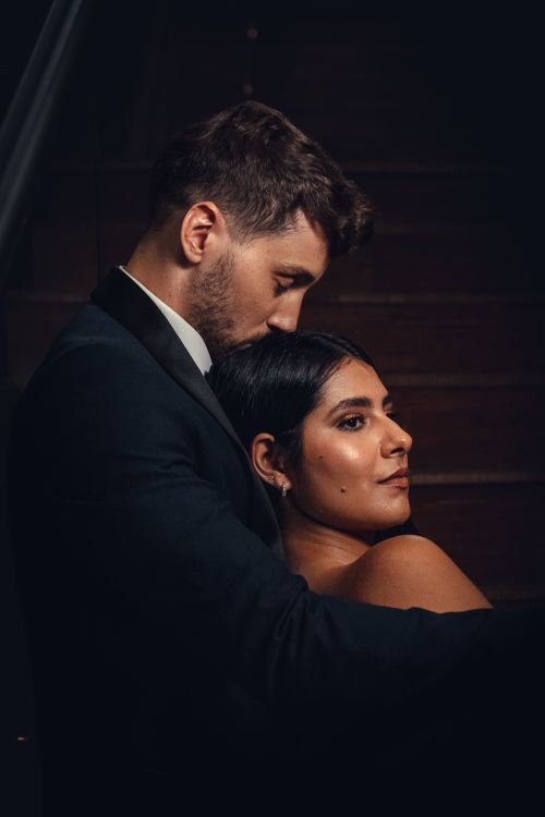 Free Elegant couple embracing on stairs in dark evening setting, conveying romance. Stock Photo