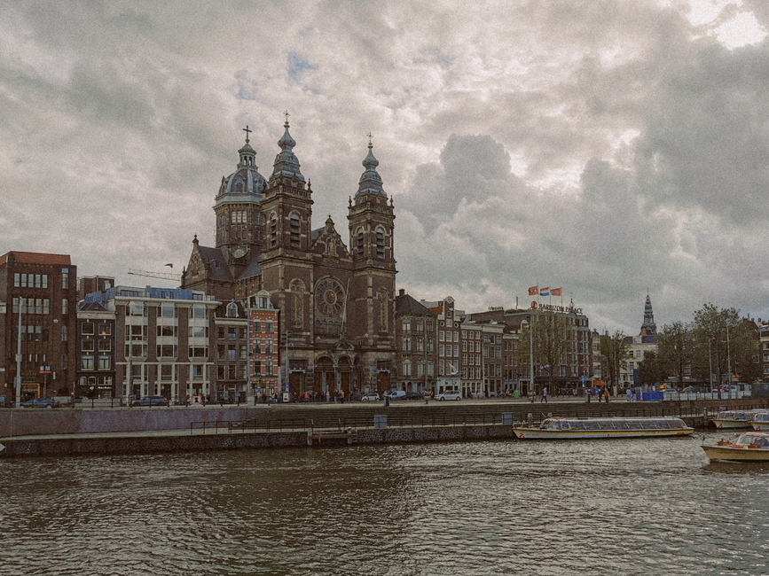 Historic Basilica of Saint Nicholas in Amsterdam with cloudy skies and canal view.