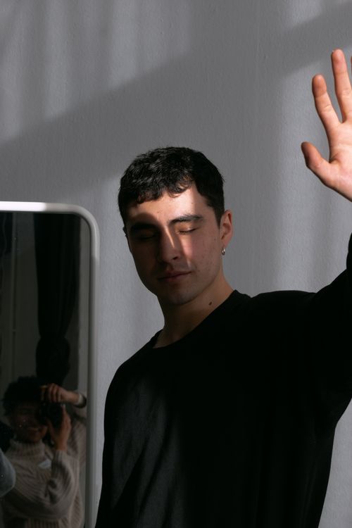 Free Portrait of a young man with eyes closed, standing in sunlight and shadow by a mirror. Stock Photo