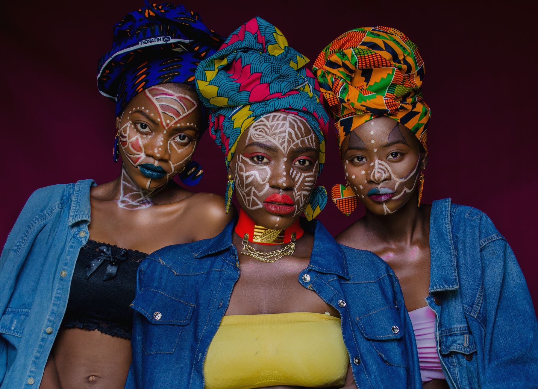Three women wearing colorful headwraps and face paint, capturing cultural vibrancy in Lagos, Nigeria.