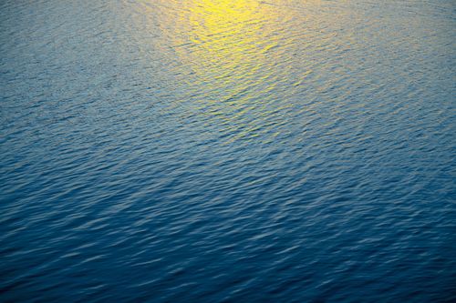 Free A tranquil scene capturing the golden reflection of sunset shimmering on a rippling blue sea. Stock Photo