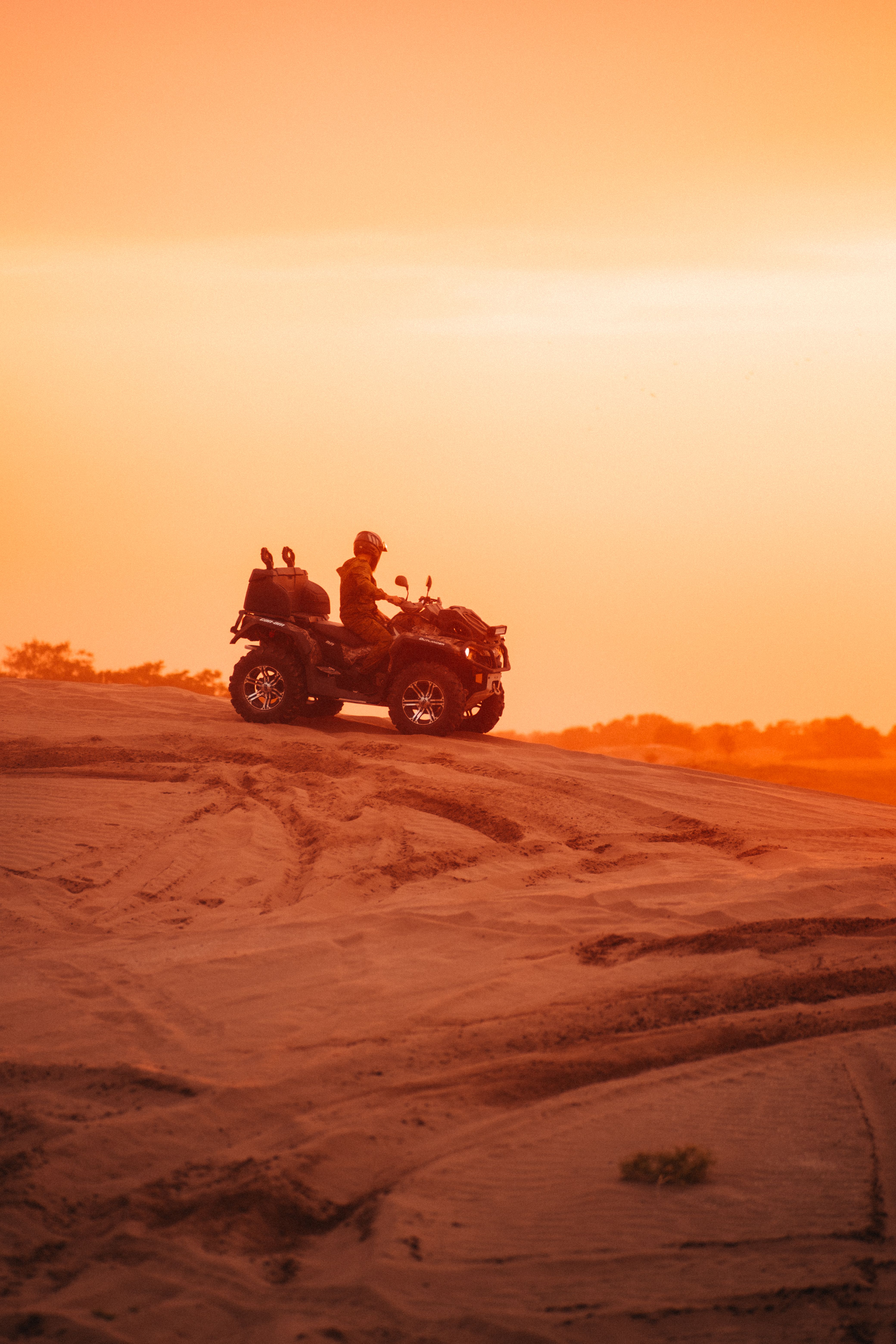 Silhouette of a person riding a quad bike on desert dunes at sunset, creating a scenic adventure vibe.