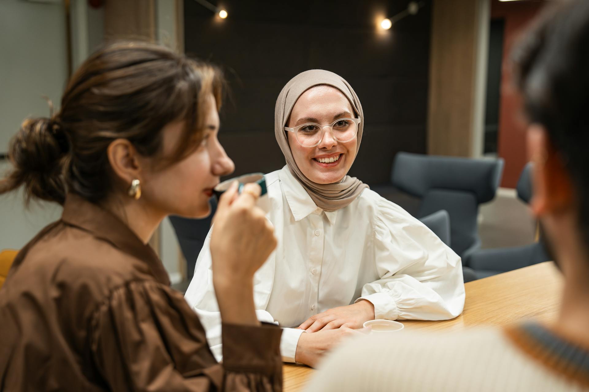 Three women enjoy a relaxed meeting in a modern office environment, engaging and smiling.