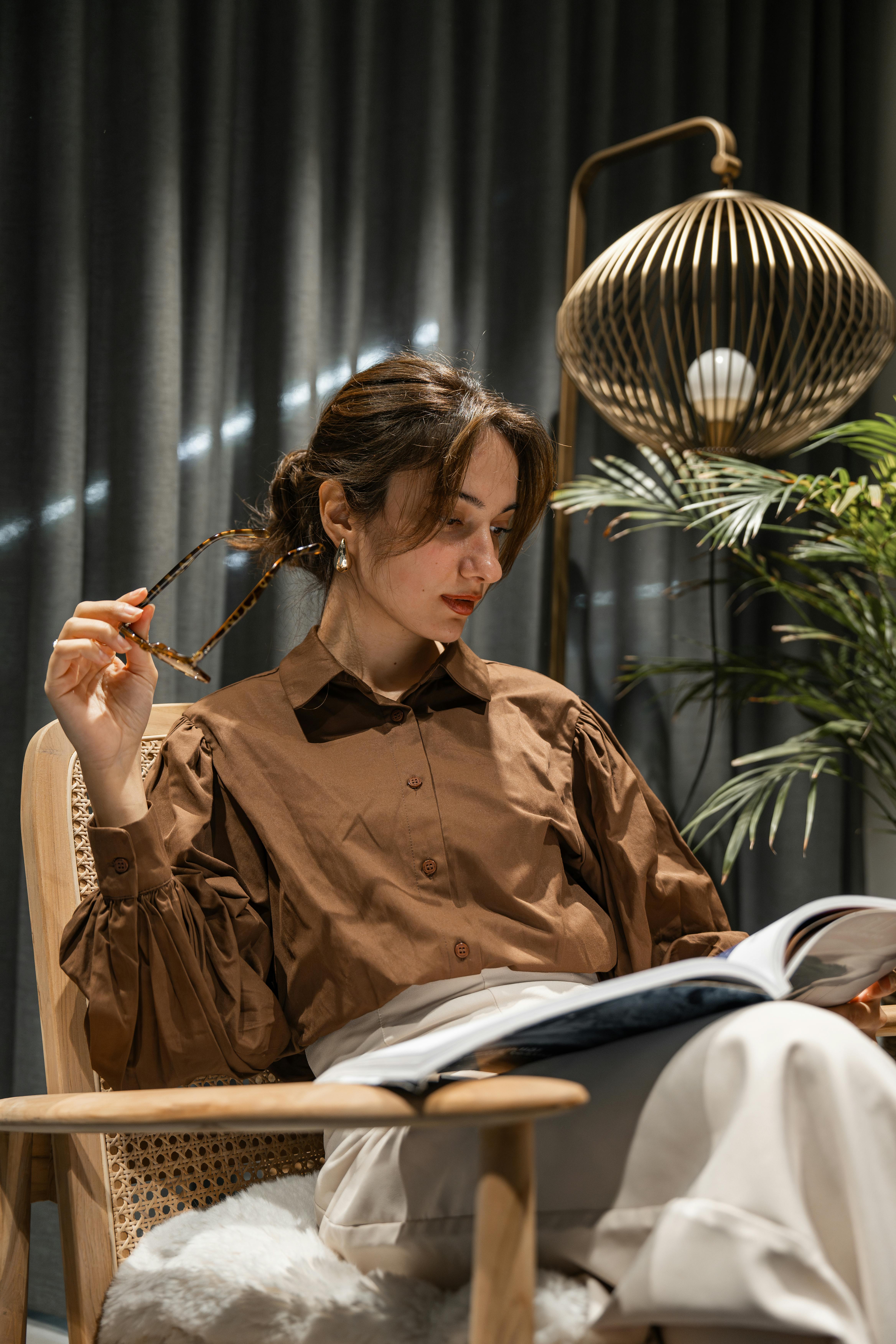 Woman sitting on a chair reading a magazine indoors, with modern decor and soft lighting.