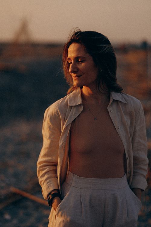 Free A woman enjoying a peaceful moment at sunset on a beach. Warm lighting creates a calm atmosphere. Stock Photo