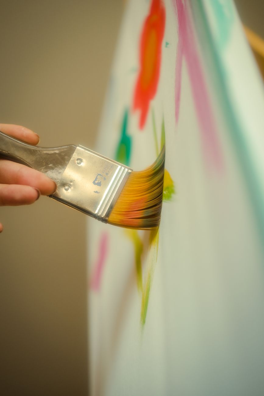 artist painting a colorful abstract canvas in a sunlit modern studio, close-up of hands with paint brushes