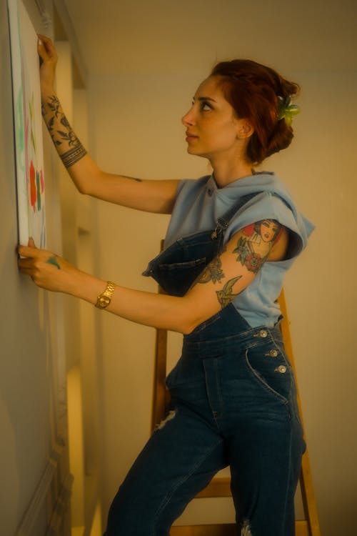 A woman with tattoos on her arm is painting on a wall