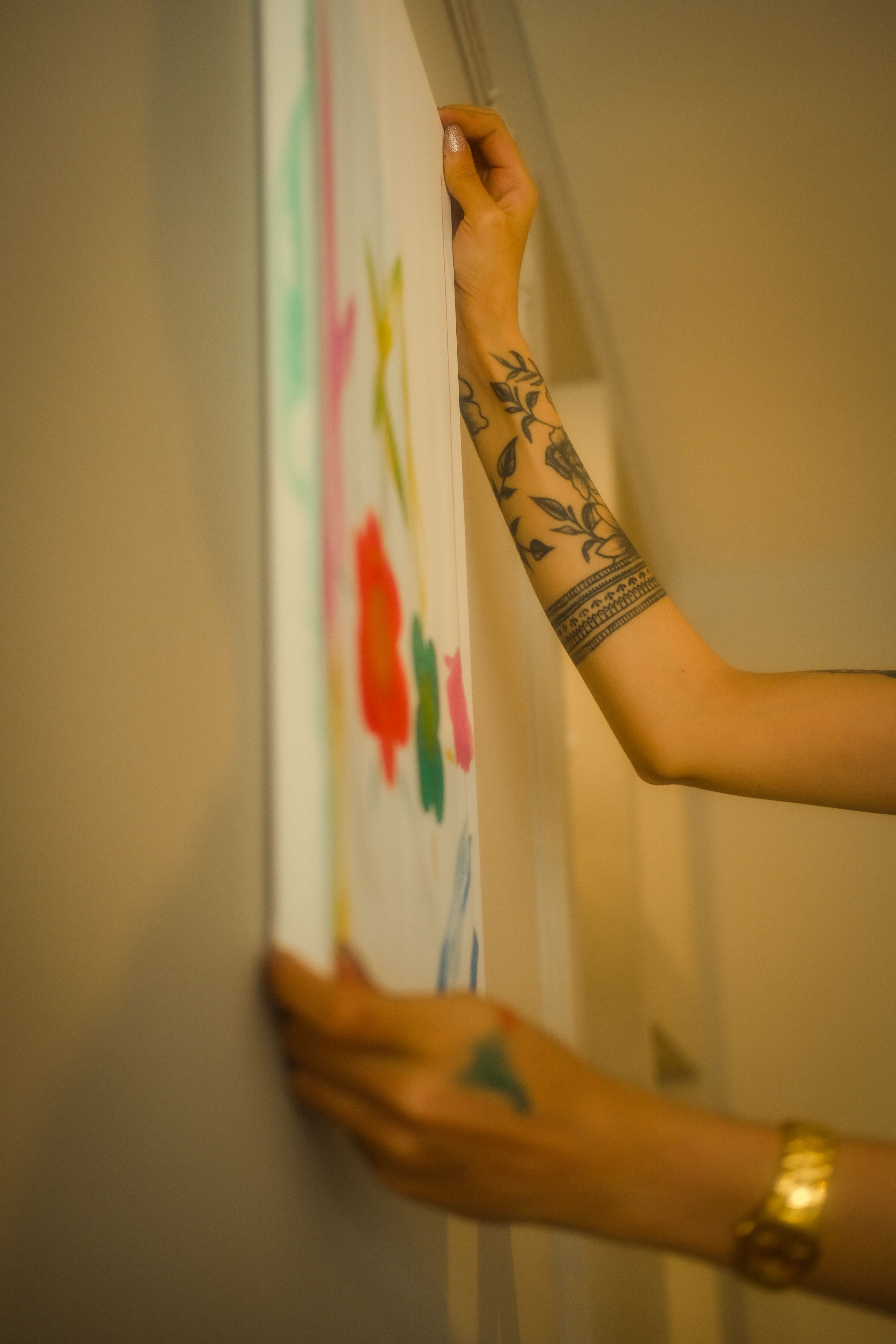 Artistic shot of a tattooed woman placing a colorful painting on a wall, showcasing creativity and personal style.