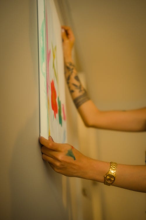 A woman with tattoos holding a painting on the wall