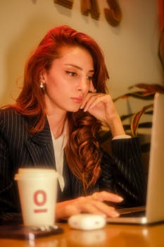 Redhead businesswoman in a suit working on a laptop with a coffee in a café.