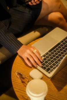 Close-up of a woman using a laptop in a cozy café, with a coffee and accessories nearby.