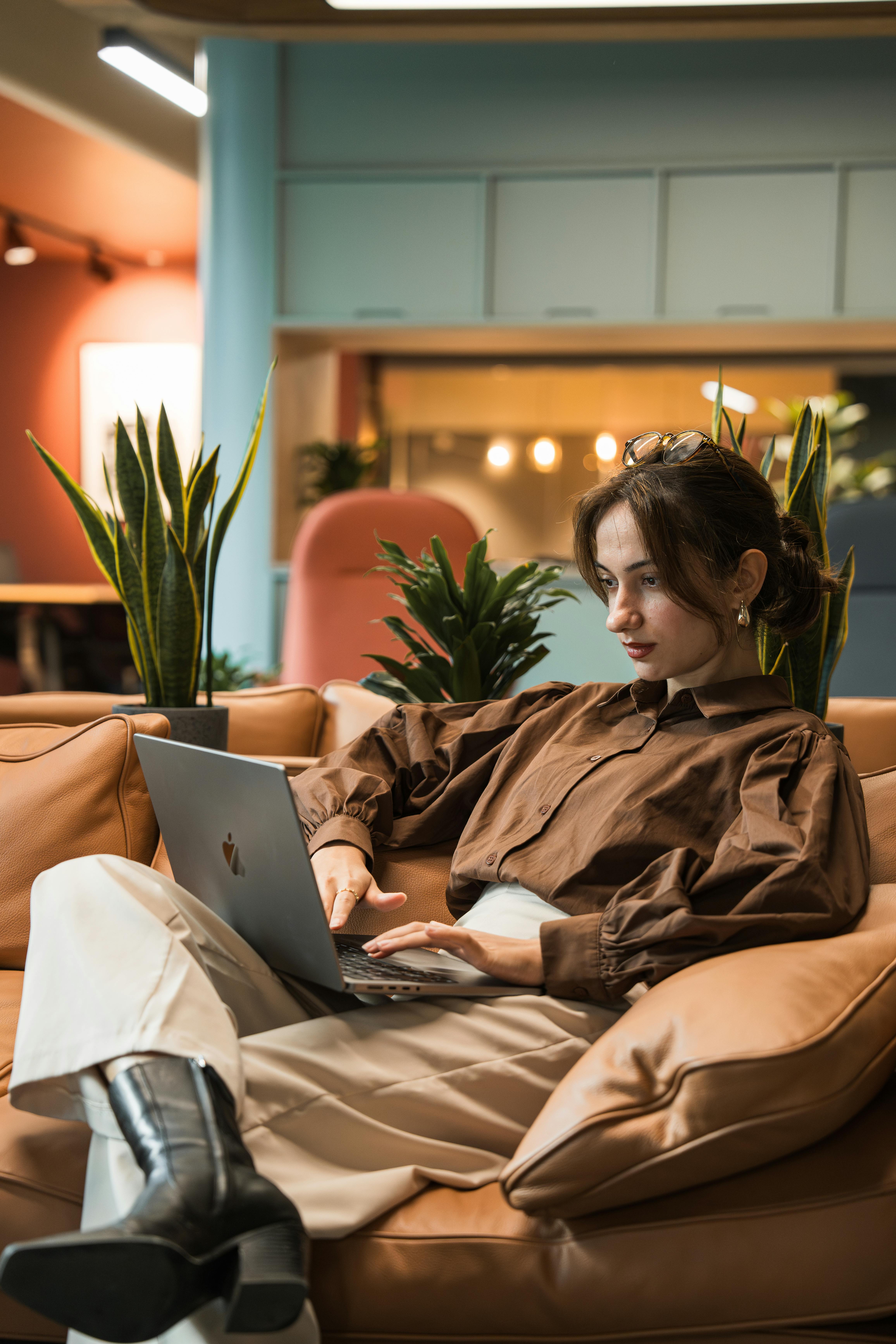 Young woman in cozy indoor setting working on her laptop amidst stylish decor and plants.