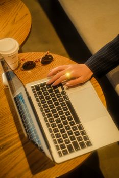 Close-up of a woman using a laptop in a cozy indoor setting with coffee and sunglasses.