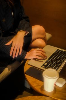 Professional woman typing on laptop in a warm, intimate setting with coffee and smartphone nearby.