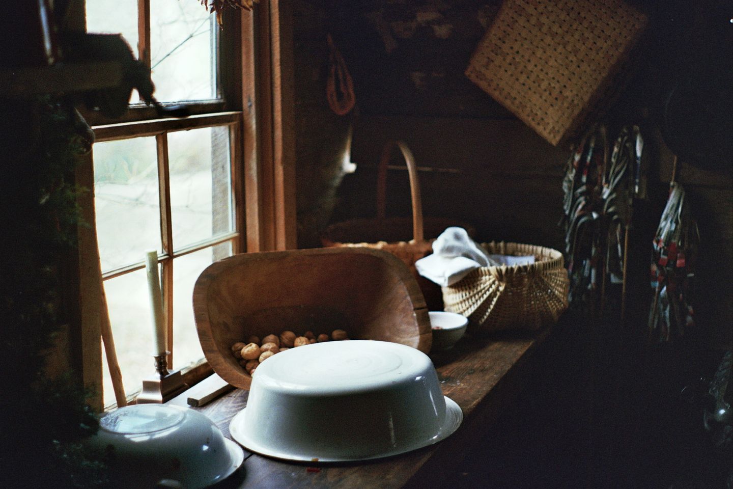 A dim country kitchen by a small-paned window, with scrubbed wood, white bowls and nothing that shouts.