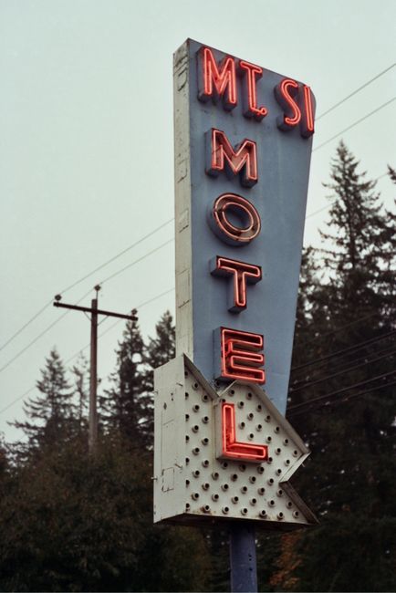 A nostalgic view of a vintage neon Mt Si Motel sign against a wooded background, evoking travel memories.