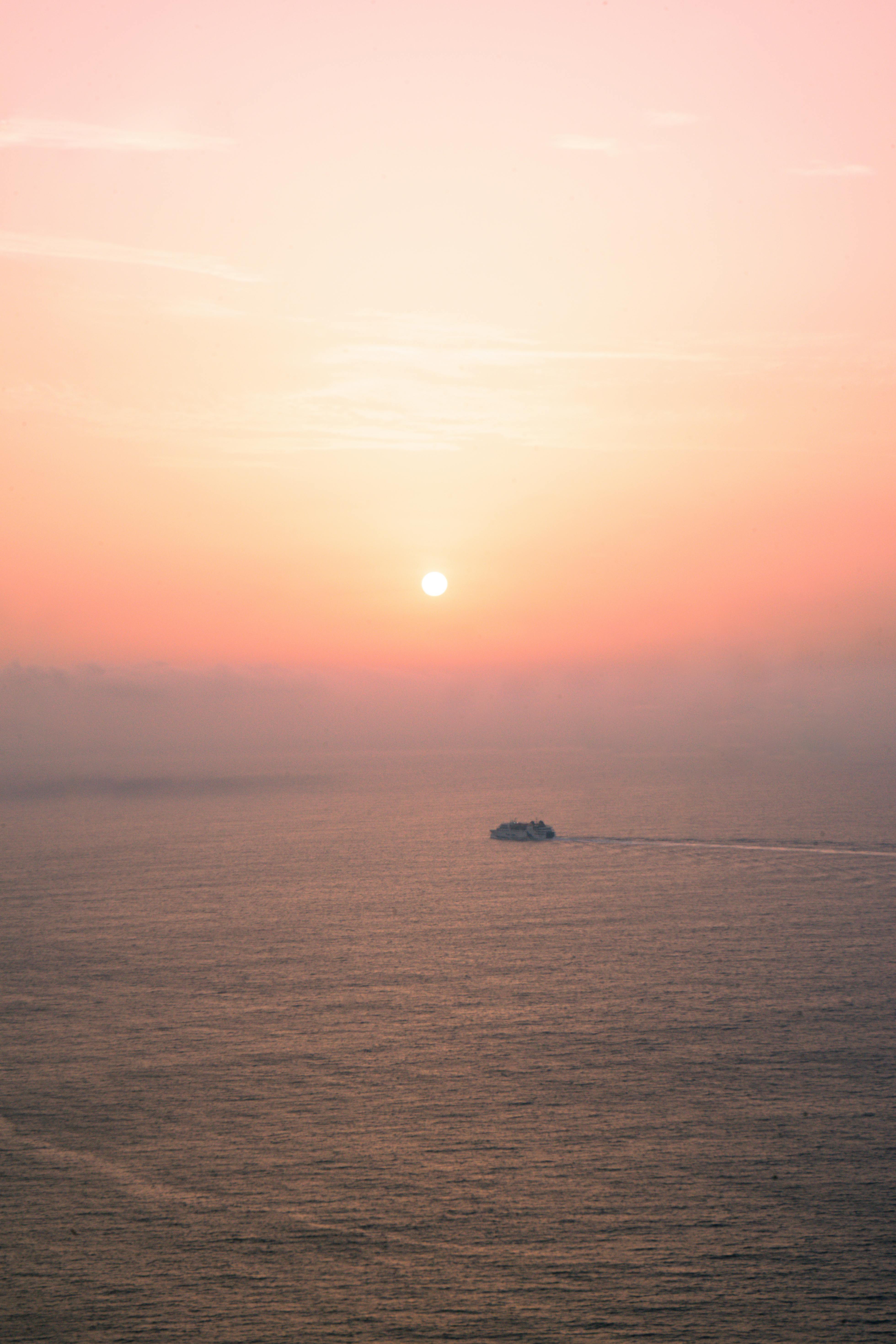 A tranquil sunrise over the ocean with a distant ship and pastel skies, creating a peaceful scene.