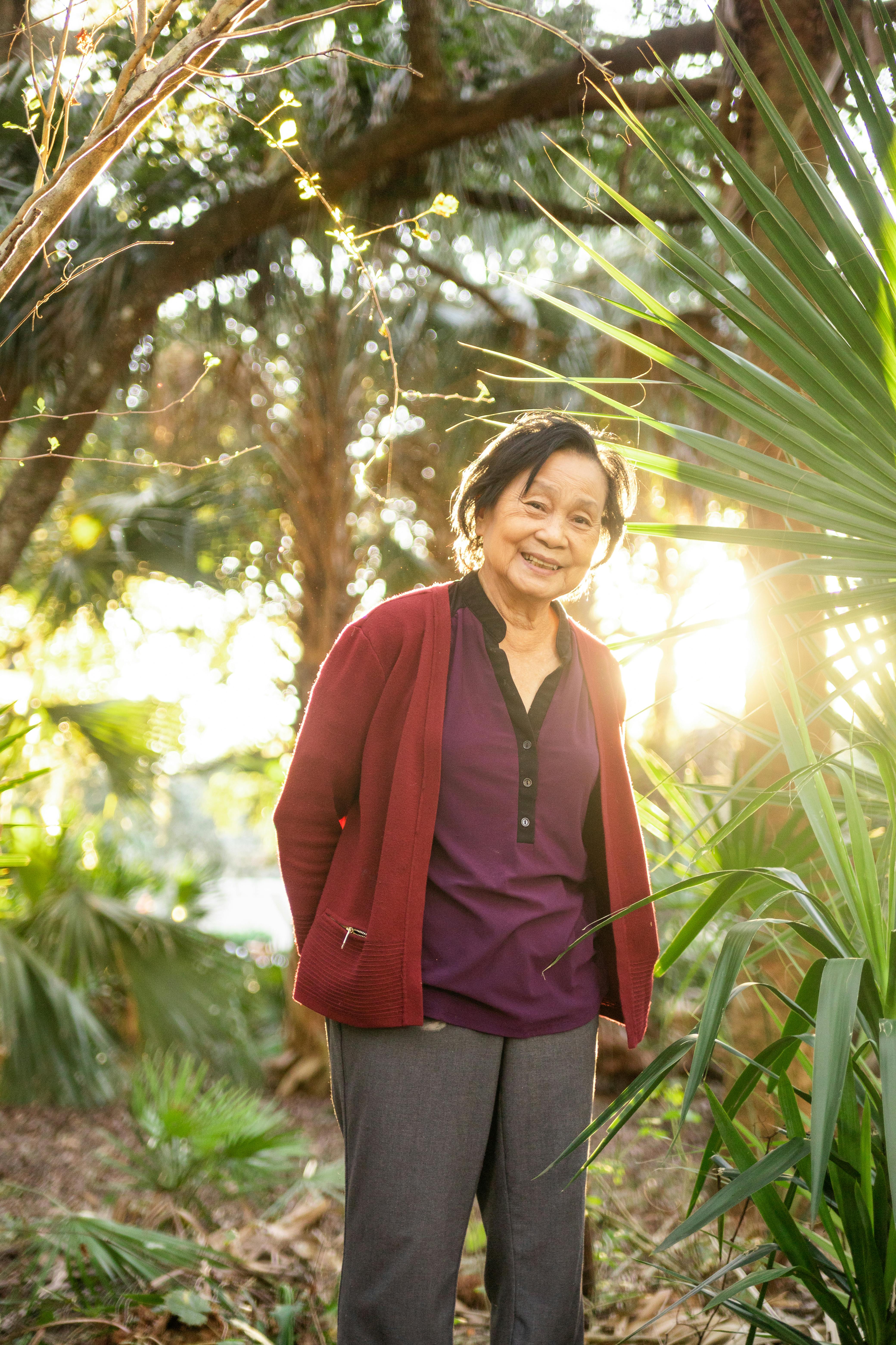 Elderly woman enjoying a sunny day in a lush garden, surrounded by greenery.