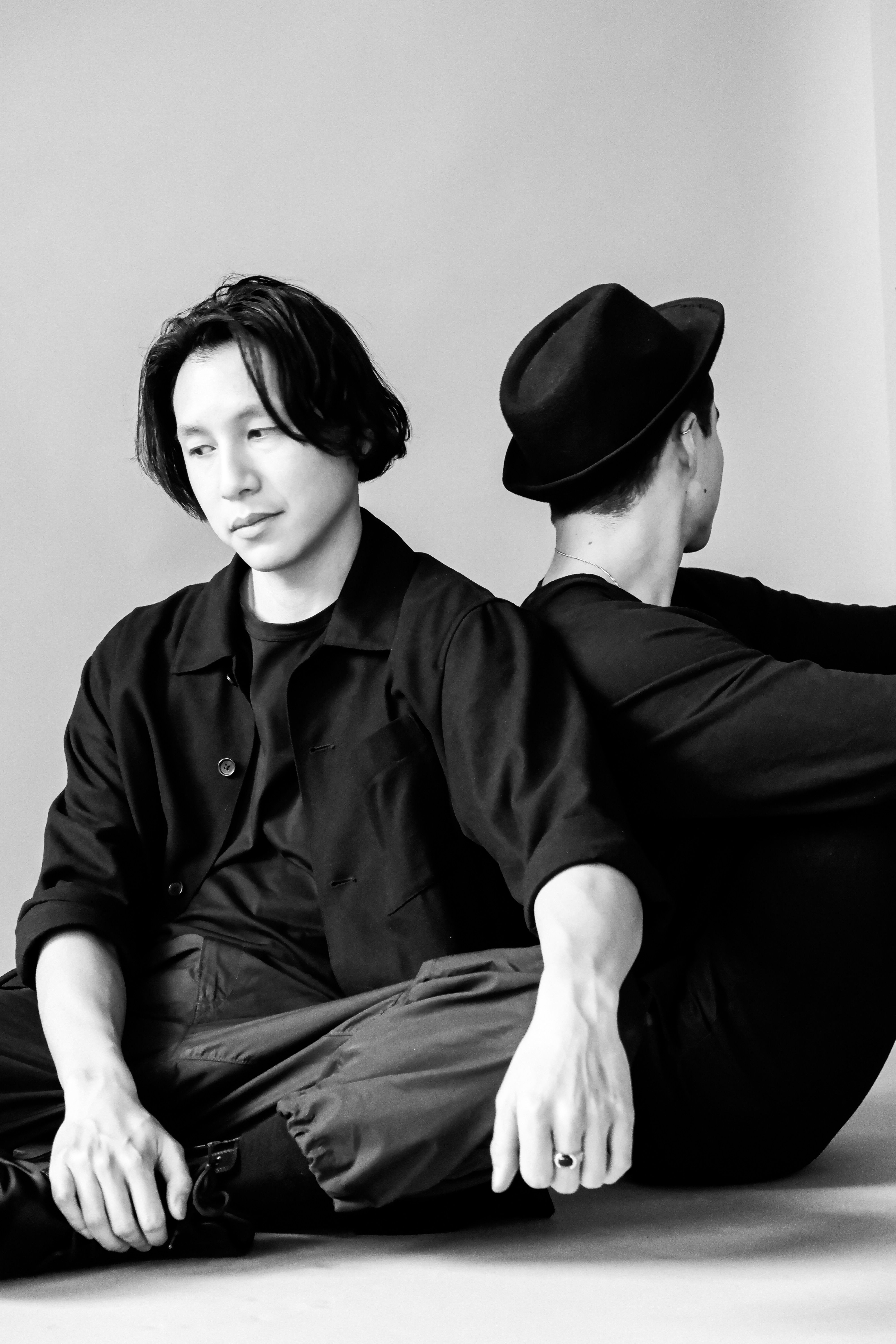 Artistic black and white studio portrait of two men sitting back to back.
