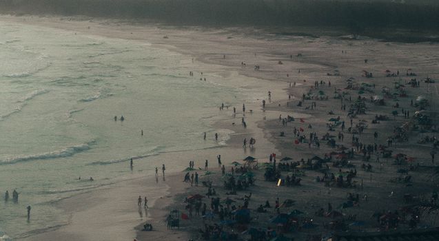 Crowded beach scene captured from above with people enjoying the shoreline at sunset.
