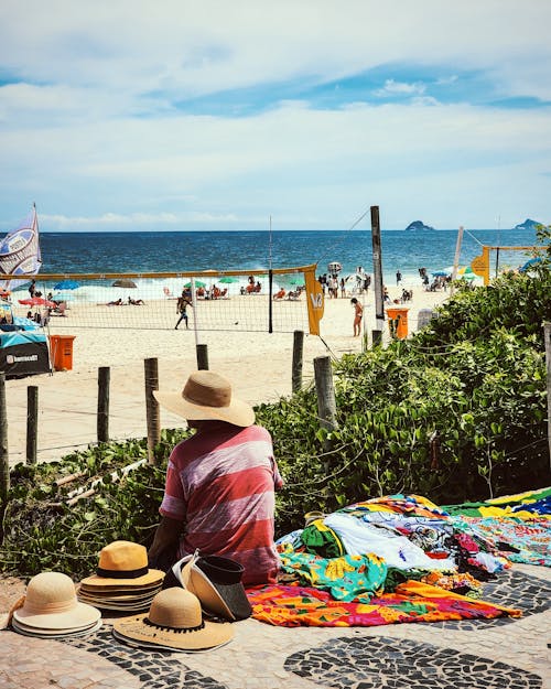 A man sitting on a beach with a hat and a blanket