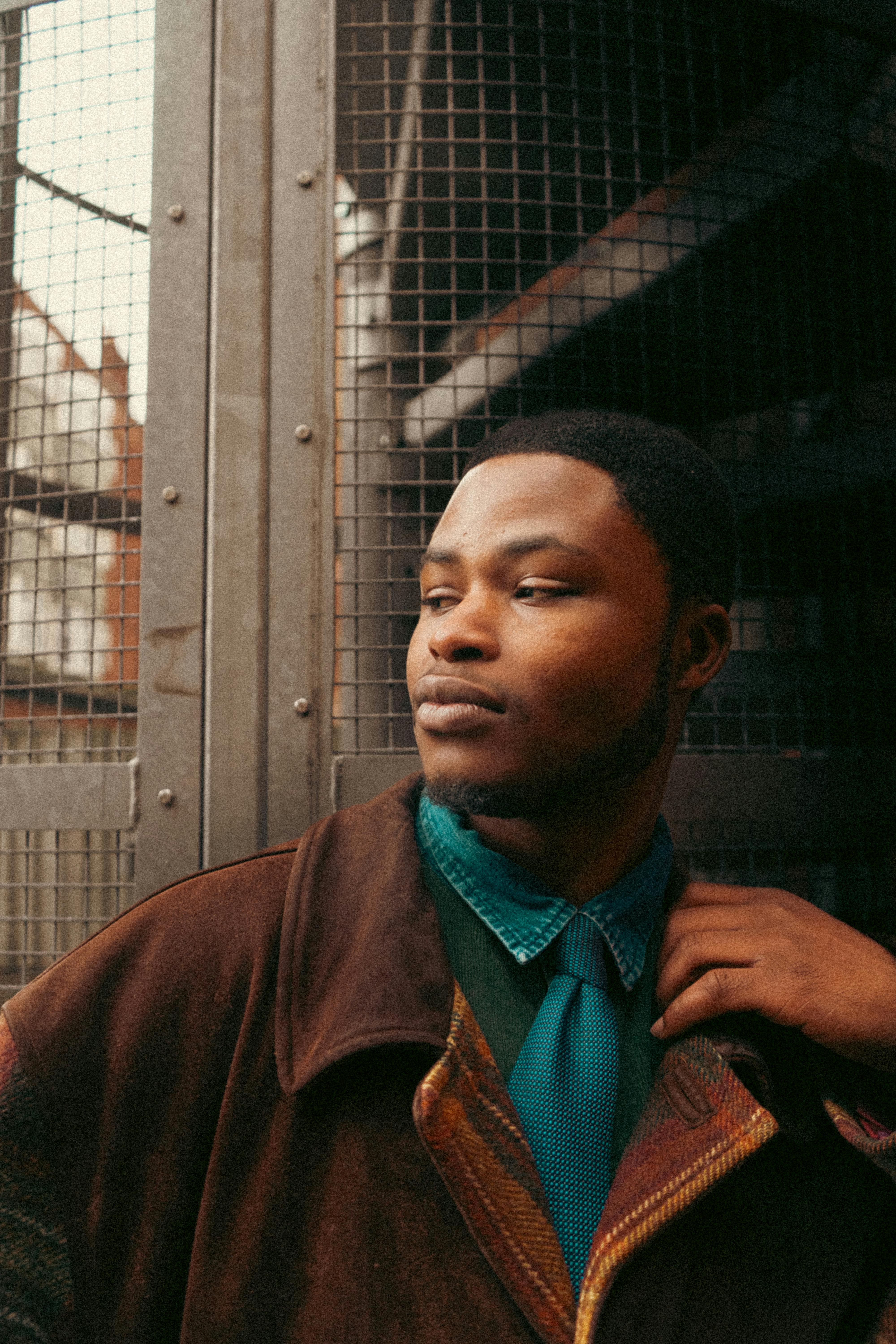 Stylish portrait of a young man in a brown jacket against an urban backdrop.