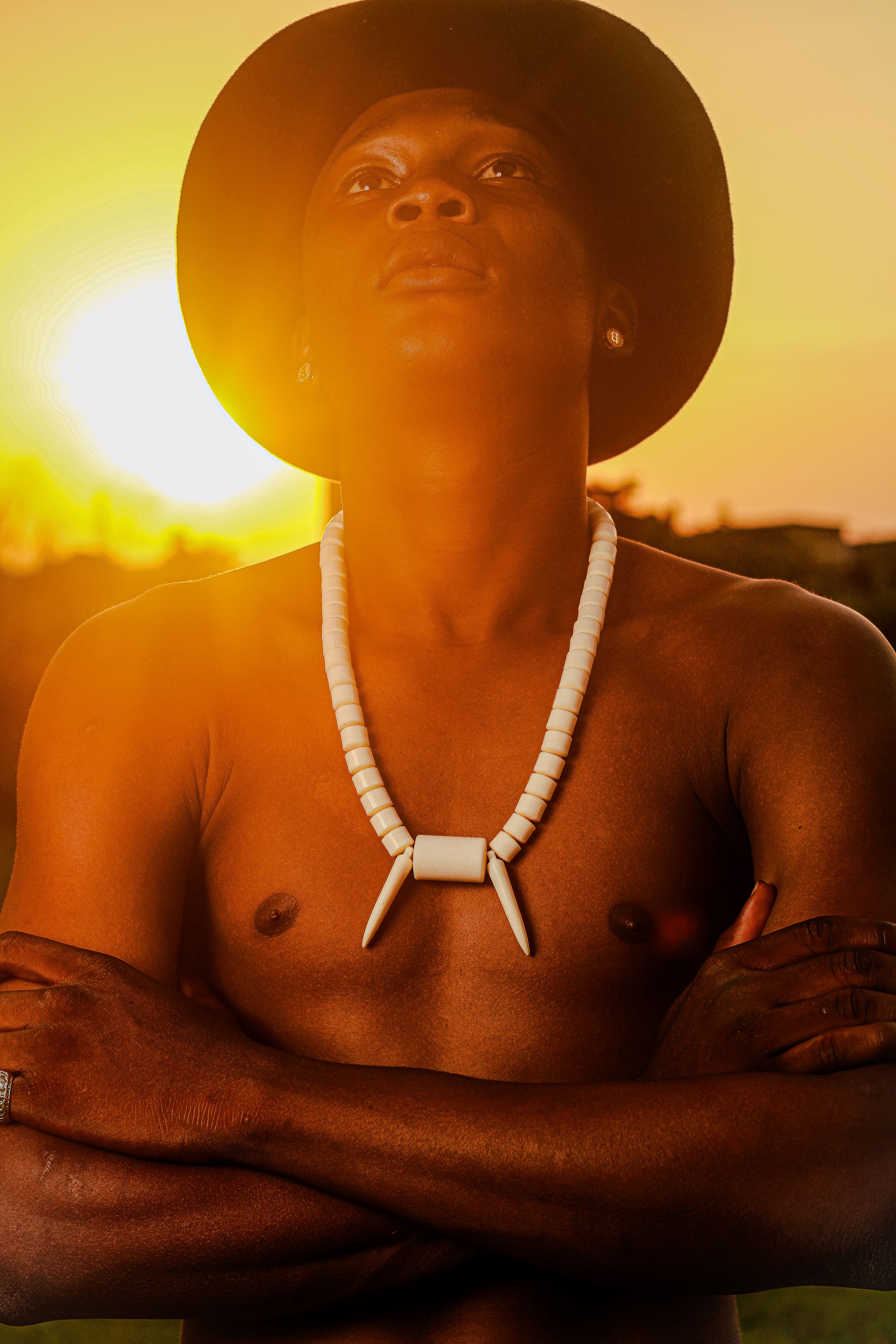 Vibrant portrait of a topless man at sunset wearing a hat and necklace.