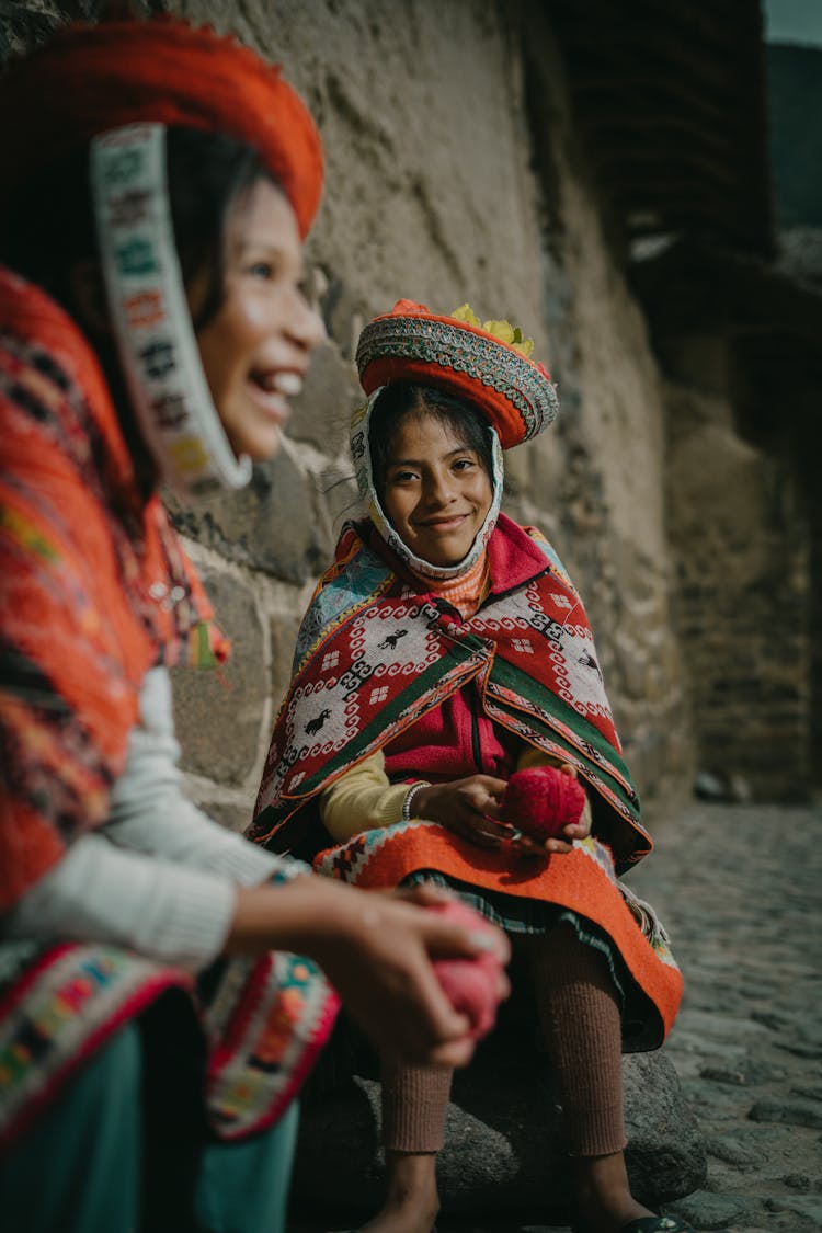 Peruvian Girls Wearing Traditional Clothing, Sitting By A Wall